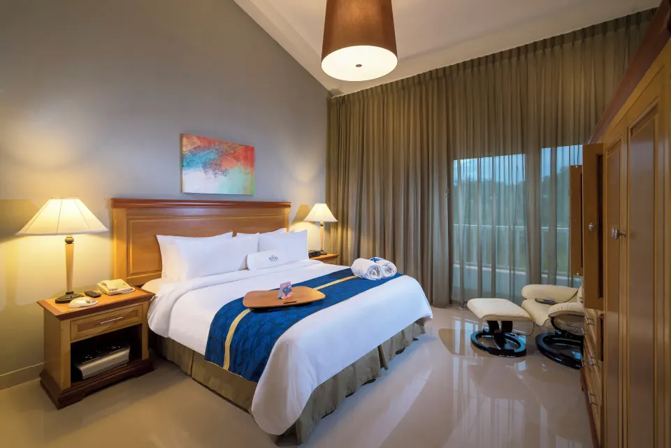 Royal Suite king bed with lamps and balcony doors at Hodelpa Garden Suites Golf & Convention Center.