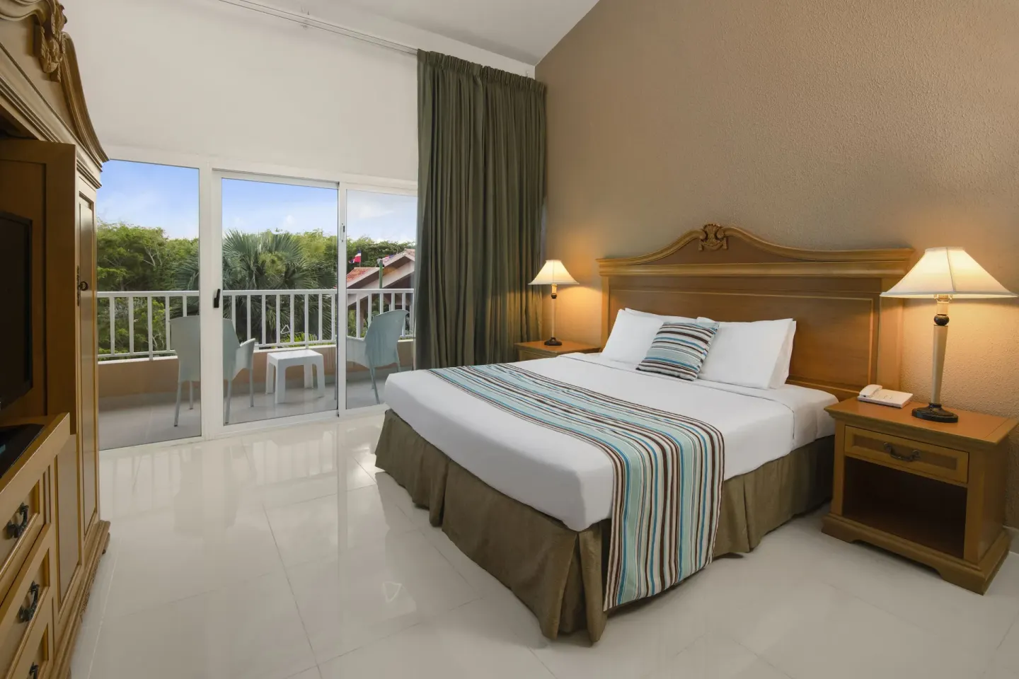 King-bed garden-view suite bedroom with balcony at Hodelpa Garden Suites Golf & Convention Center.
