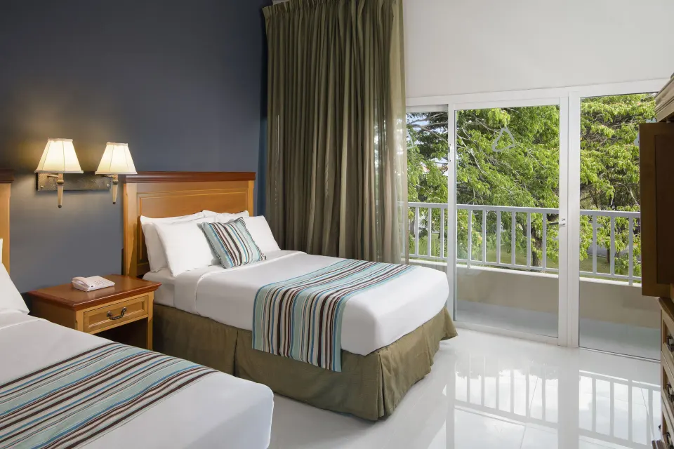 Two-bed garden-view suite bedroom with balcony doors at Hodelpa Garden Suites Golf & Convention Center.
