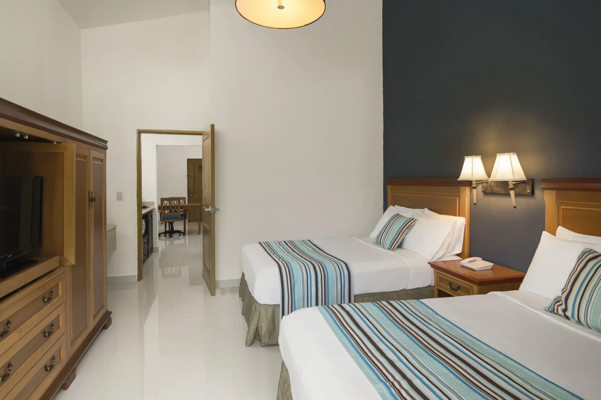 Two-bed garden-view suite bedroom with wood armoire at Hodelpa Garden Suites Golf & Convention Center.