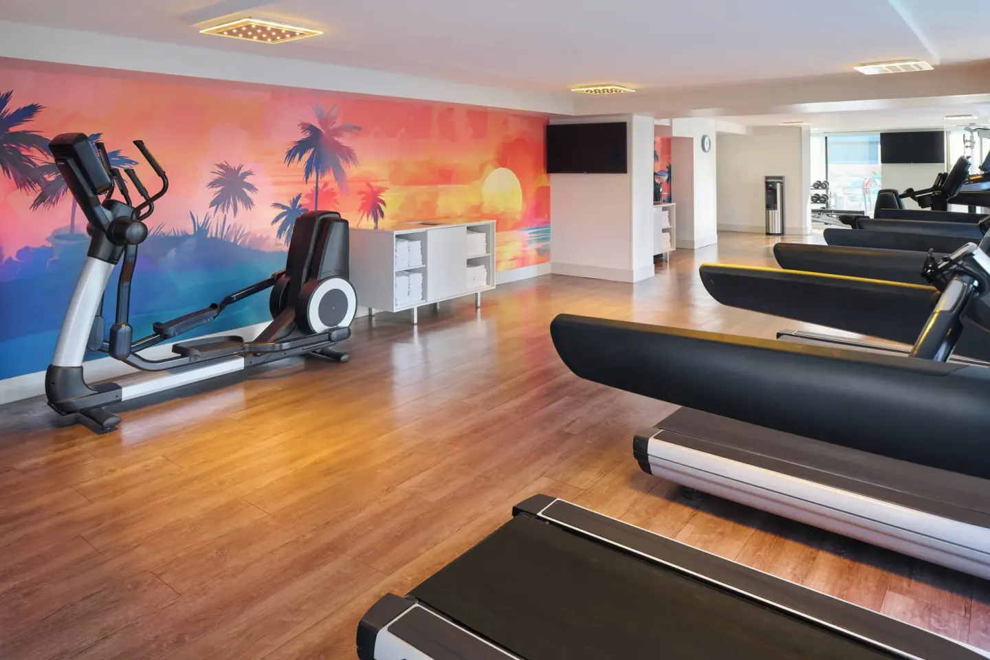 Fitness room with treadmills and a sunset palm mural at Holiday Inn Express Waikiki.