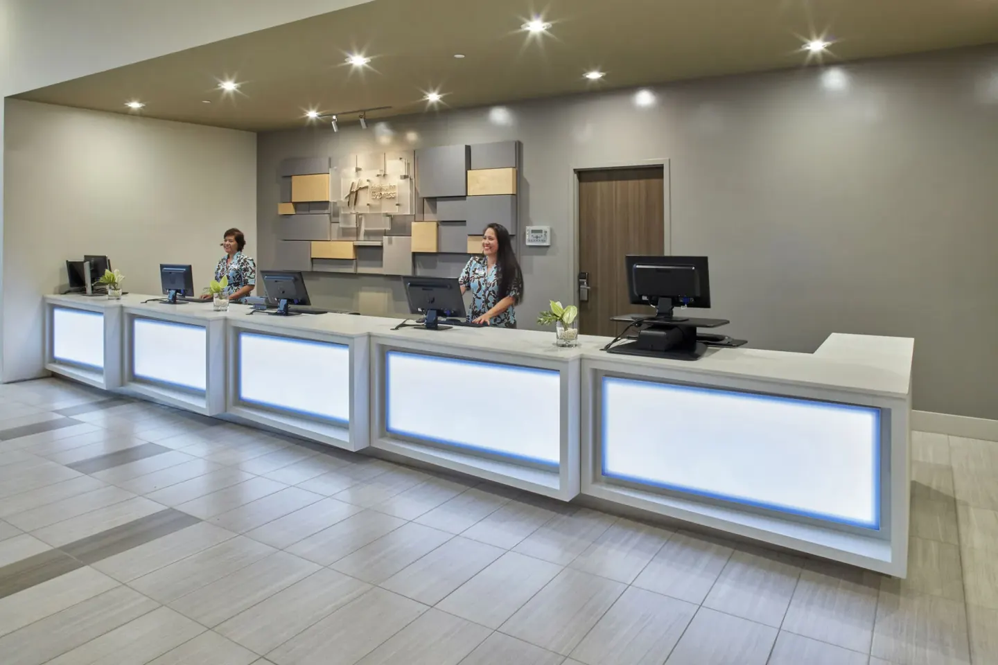 Front desk with illuminated counters and two staff members at Holiday Inn Express Waikiki.