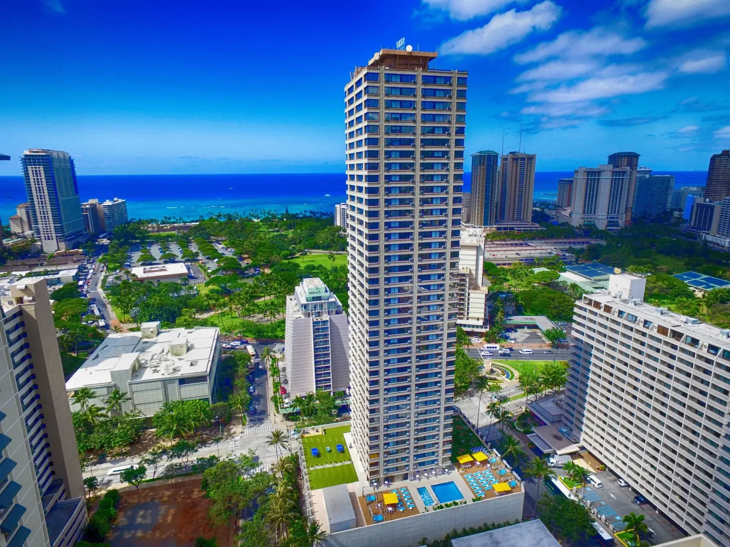 Aerial view of the Holiday Inn Express Waikiki tower with pool deck and ocean beyond.
