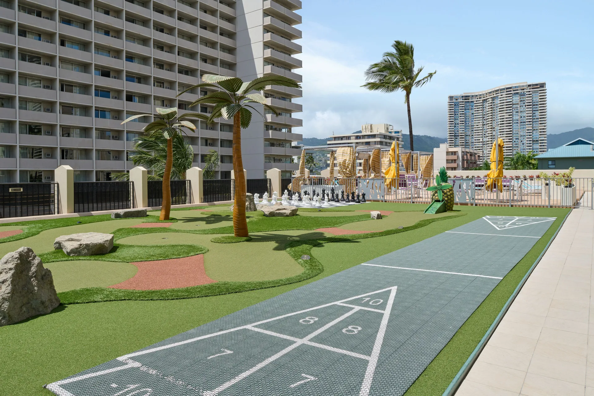 Outdoor game area at Holiday Inn Express Waikiki with shuffleboard, putting green, chess, and city views.