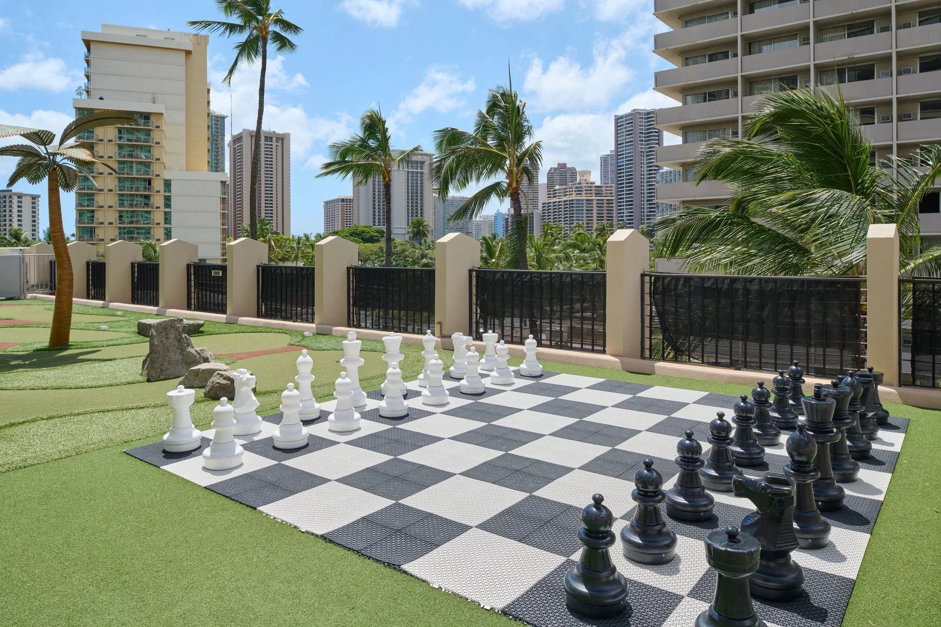 Outdoor giant chess set on turf with city buildings near Holiday Inn Express Waikiki.