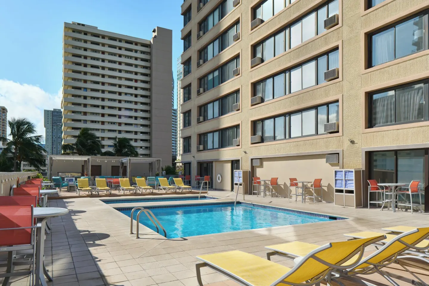 Outdoor pool area with yellow loungers and city buildings at Holiday Inn Express Waikiki.
