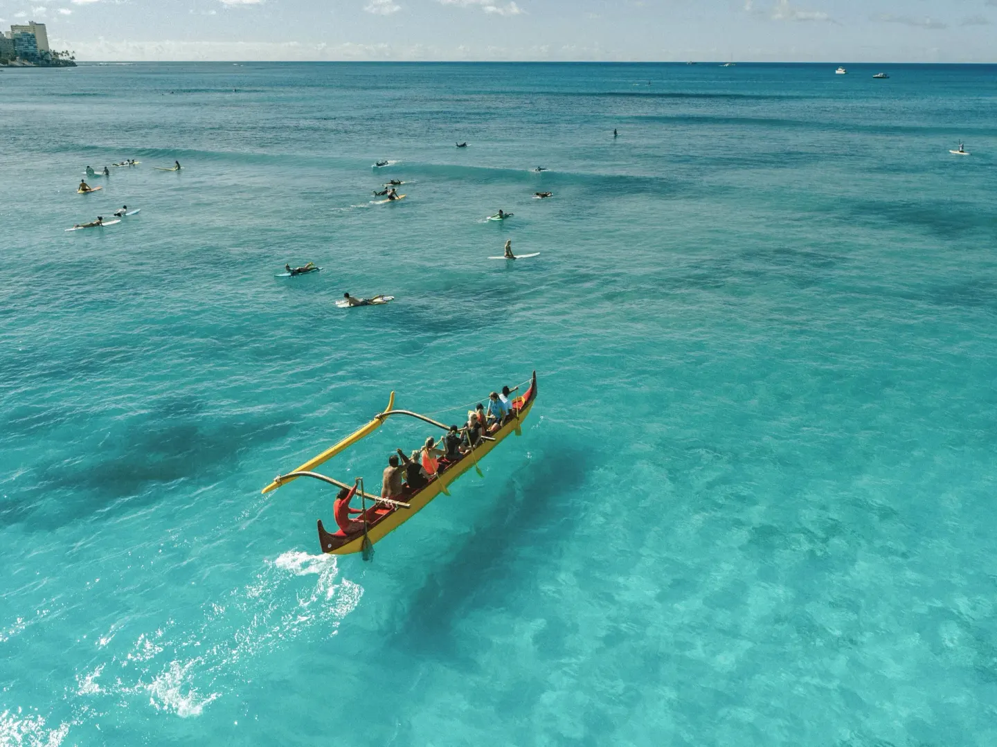 Outrigger canoe and surfers on clear turquoise water near Holiday Inn Express Waikiki.