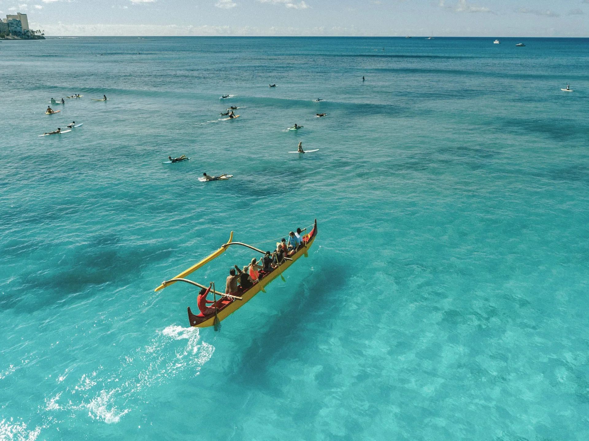 Outrigger canoe and surfers on clear turquoise water near Holiday Inn Express Waikiki.