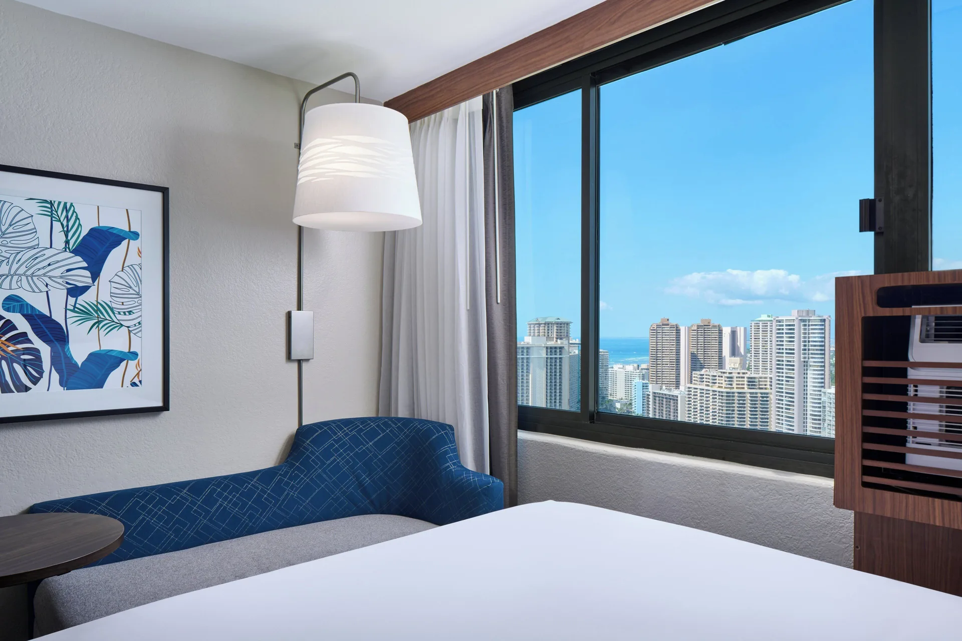 Standard Room partial ocean view seating area and bed at Holiday Inn Express Waikiki.