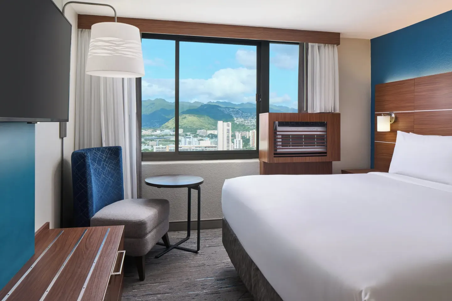 Standard Room king bed with mountain-facing window and chair at Holiday Inn Express Waikiki.