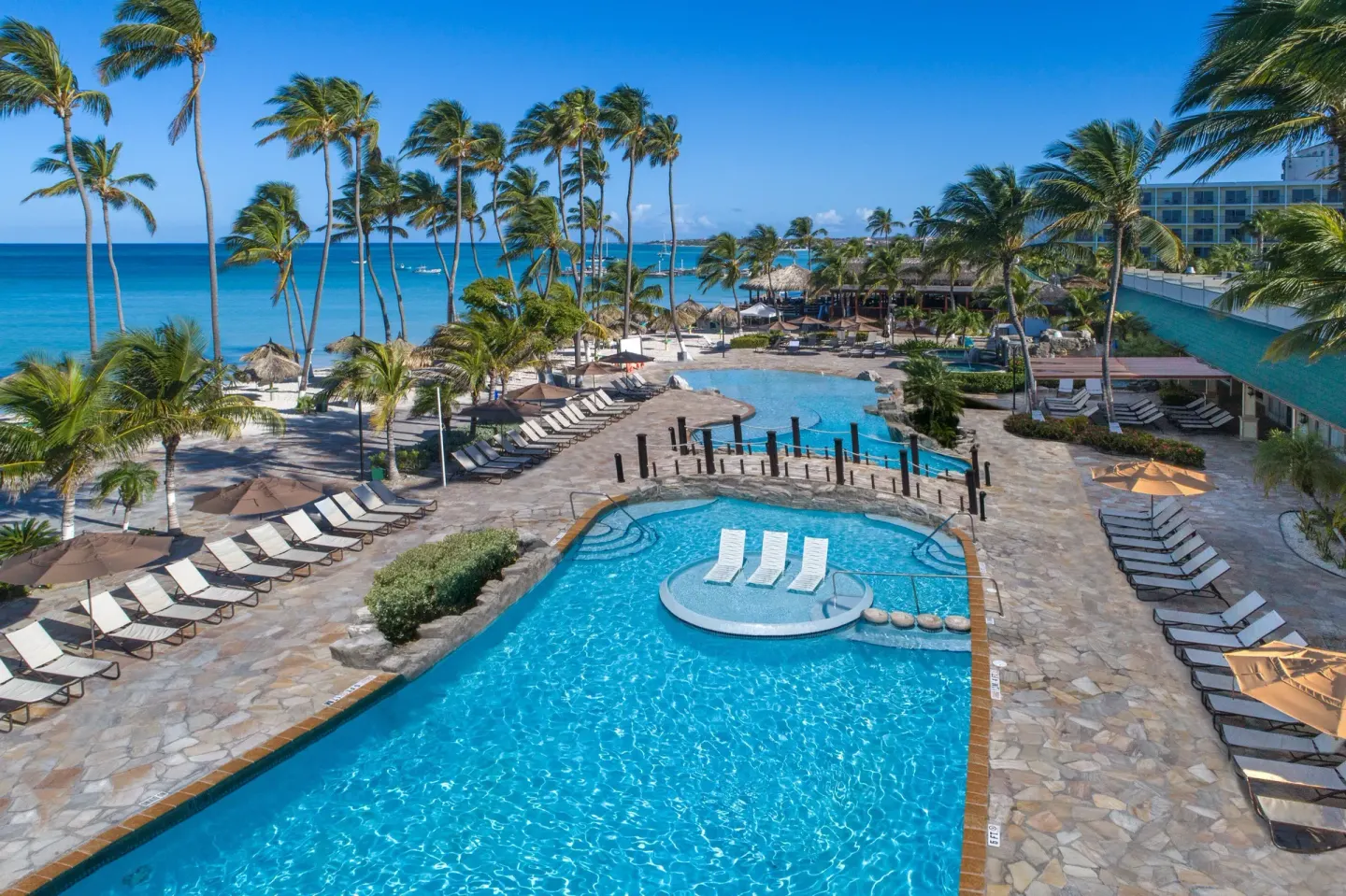 Elevated view of pools, loungers, palms, and beach at Holiday Inn Resort Aruba - Beach Resort & Casino.