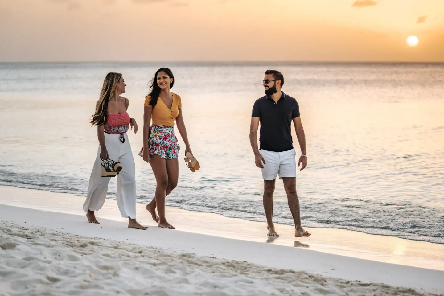 Three people walk on the beach at sunset at Holiday Inn Resort Aruba - Beach Resort & Casino.