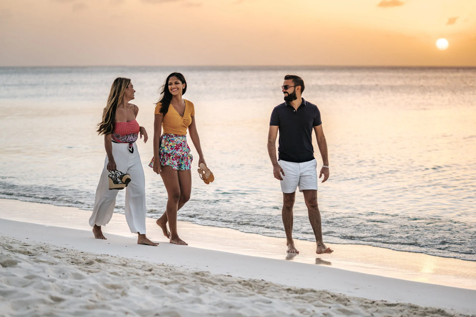 Three people walk on the beach at sunset at Holiday Inn Resort Aruba - Beach Resort & Casino.