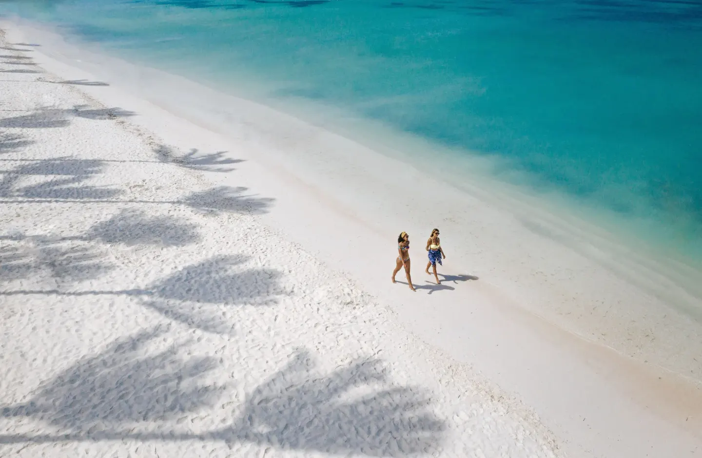 Two people walk along the white-sand beach at Holiday Inn Resort Aruba - Beach Resort & Casino.