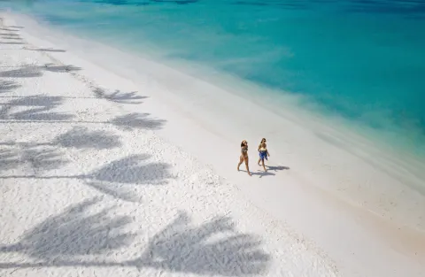 Two people walk along the white-sand beach at Holiday Inn Resort Aruba - Beach Resort & Casino.