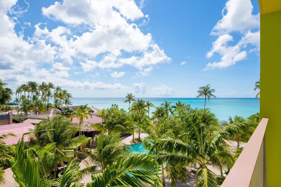 Balcony view with palms, pool, and ocean at Holiday Inn Resort Aruba - Beach Resort & Casino.