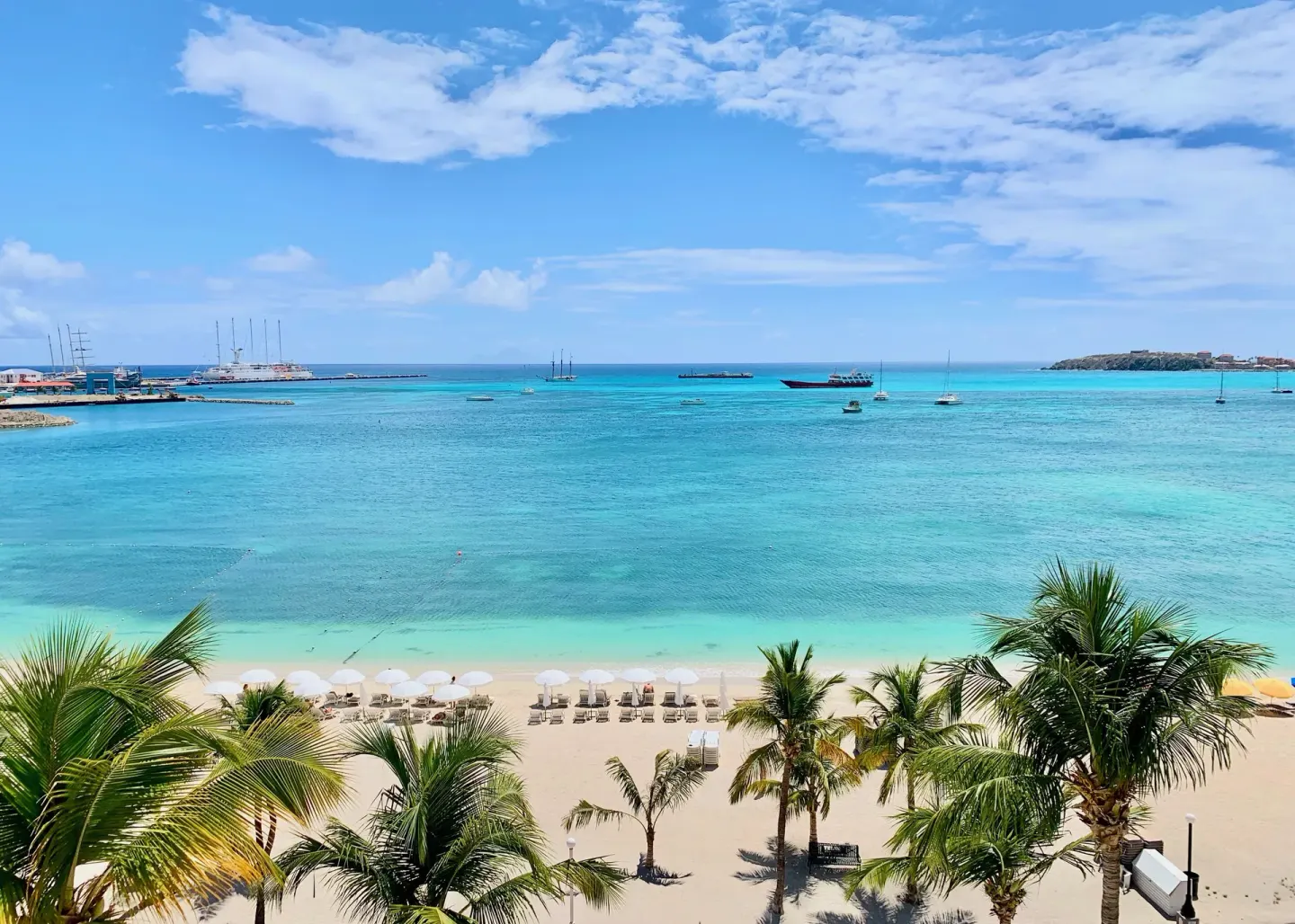 Beach loungers, palms, and turquoise bay at Holland House Beach Hotel.