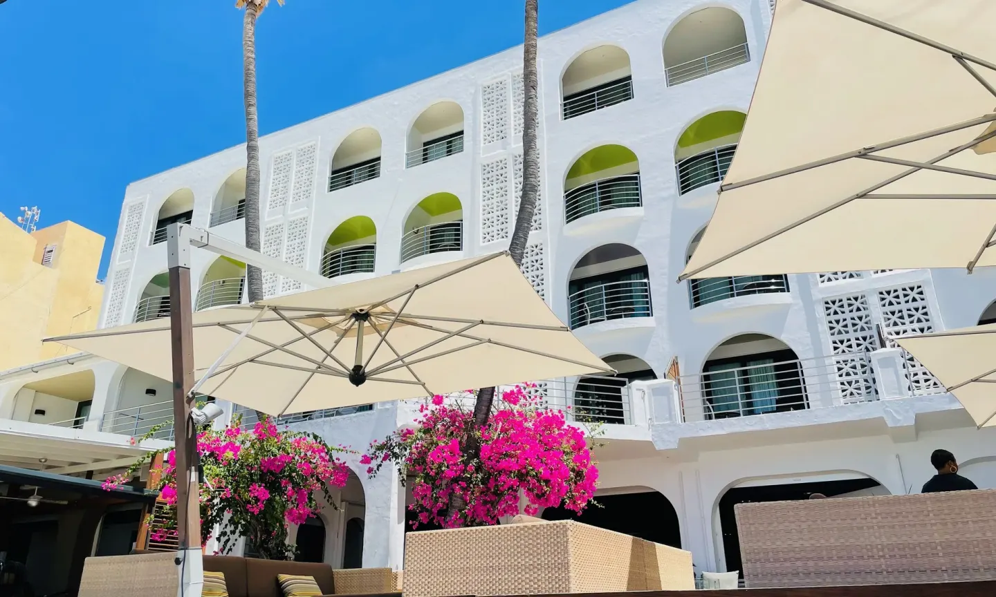 White arched balconies rise above umbrellas and bougainvillea at Holland House Beach Hotel.