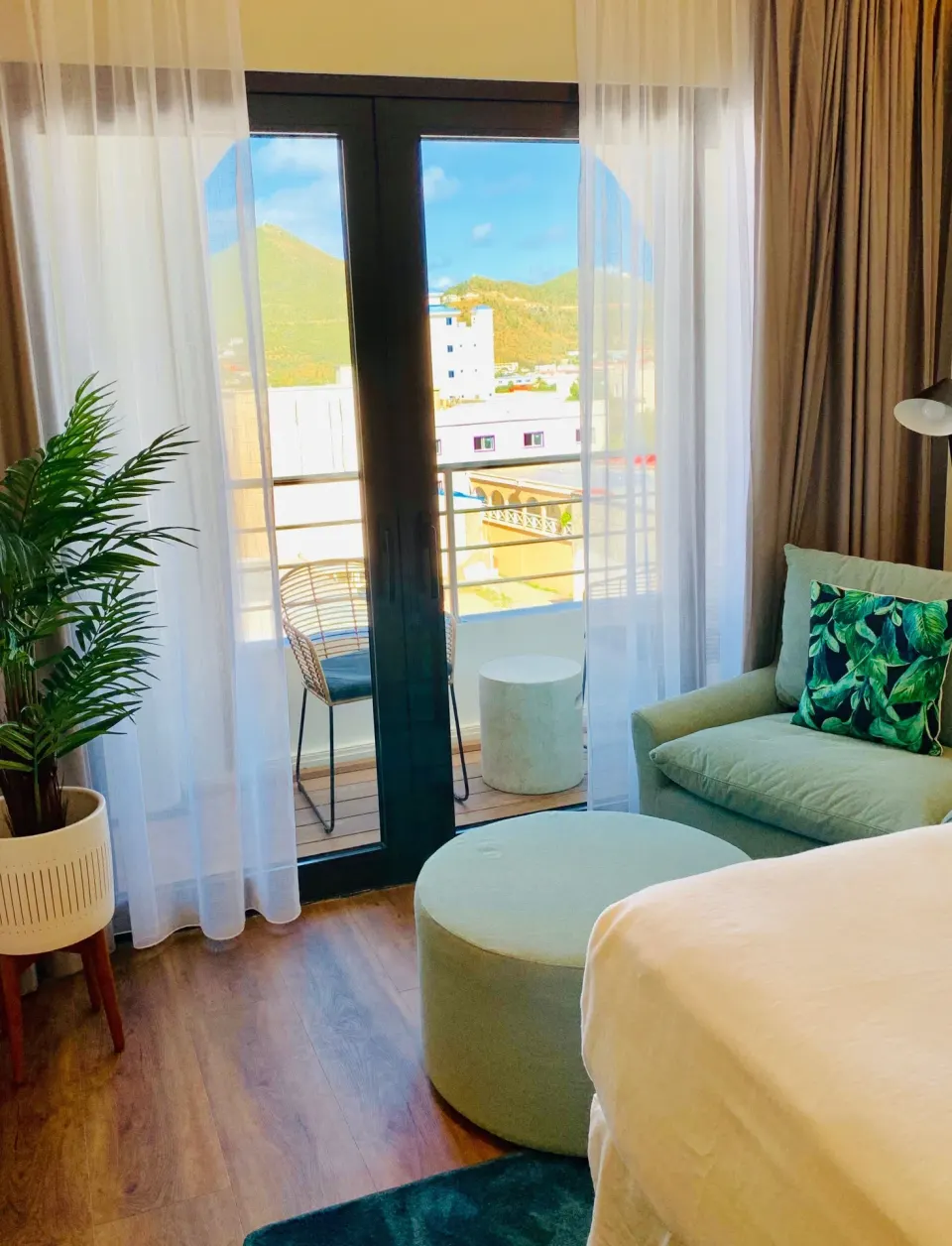 Guest room sitting area at Holland House Beach Hotel with balcony doors, sheer curtains, and a bed edge.