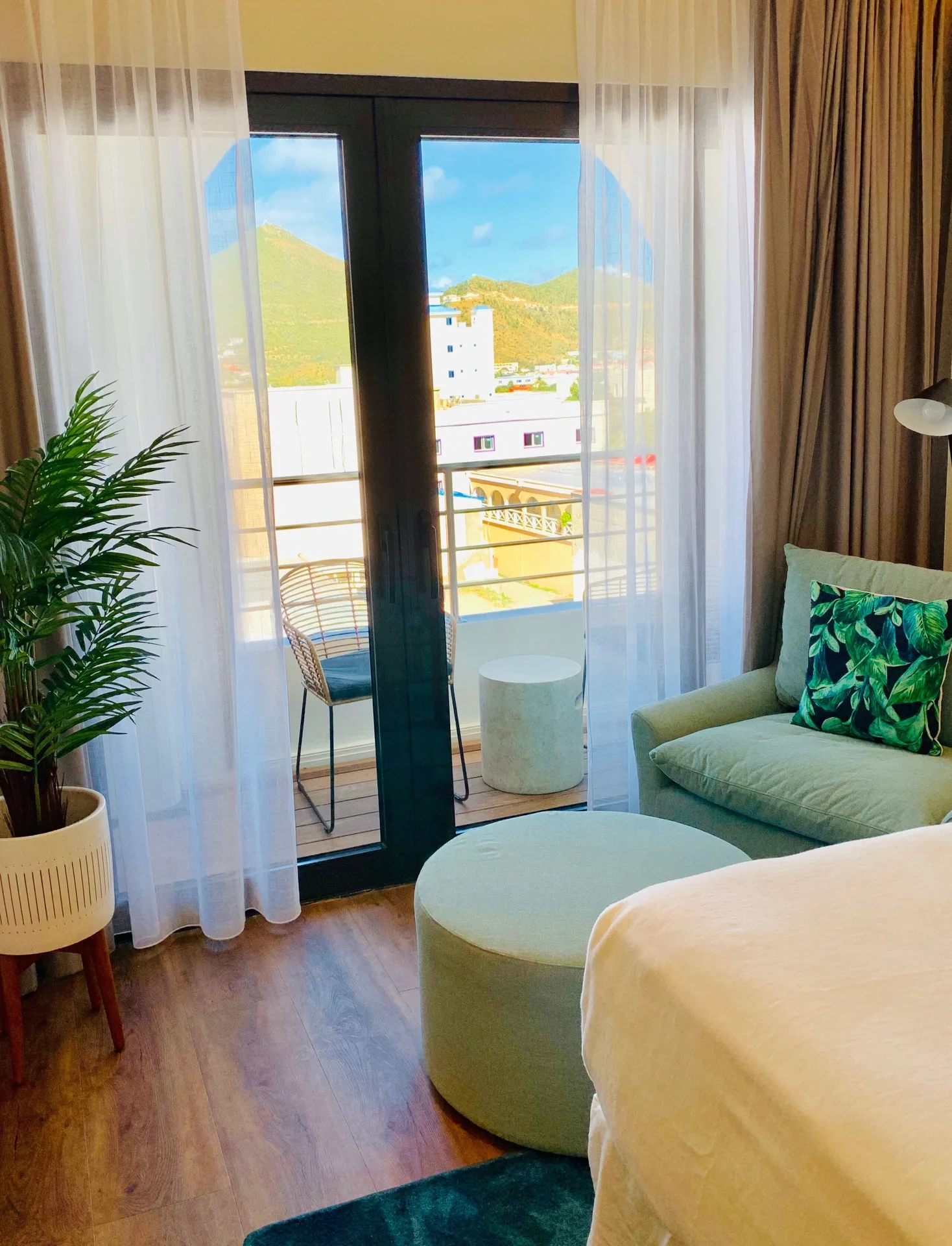 Guest room sitting area at Holland House Beach Hotel with balcony doors, sheer curtains, and a bed edge.