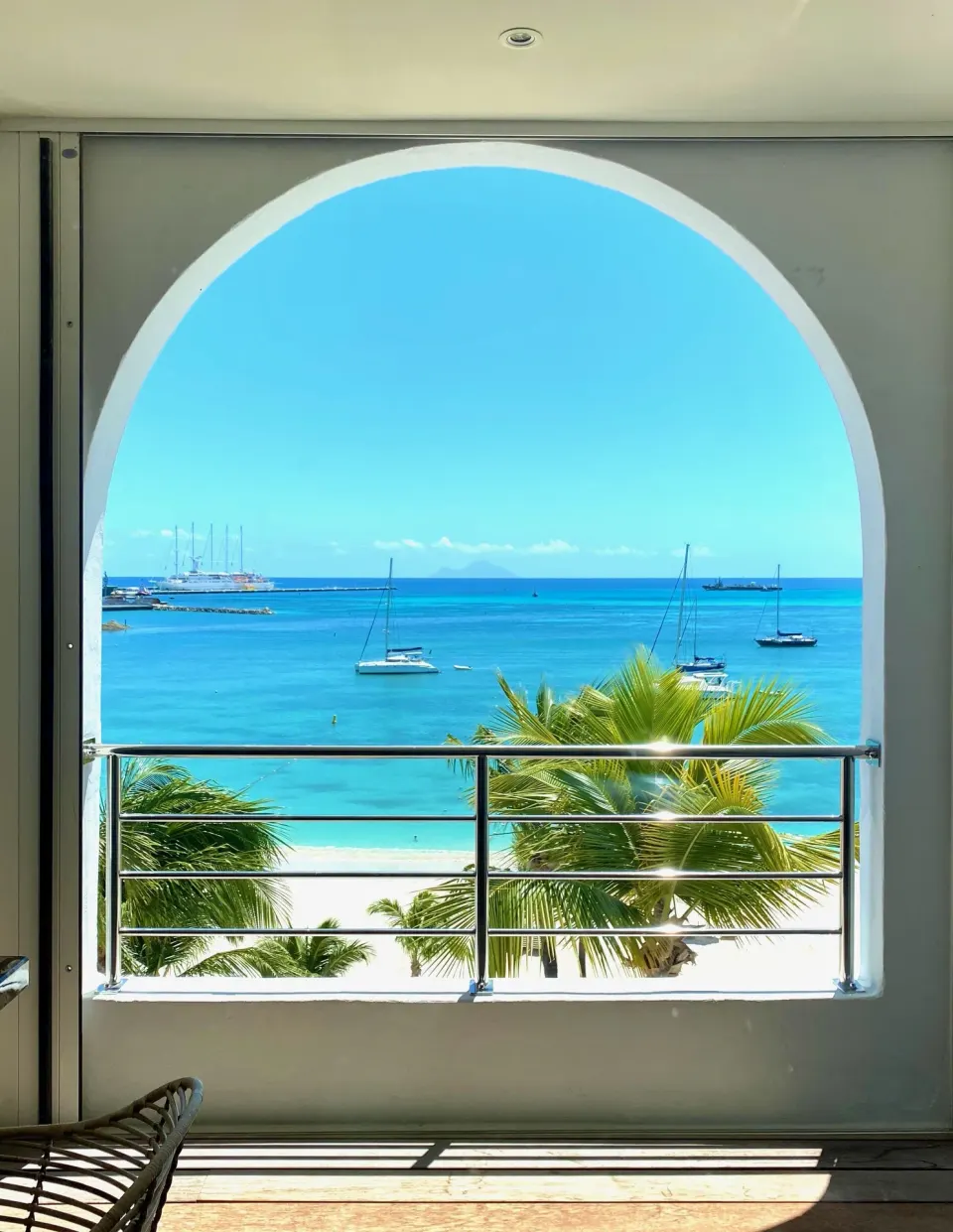 Arched balcony view of palms, beach, and boats at Holland House Beach Hotel.