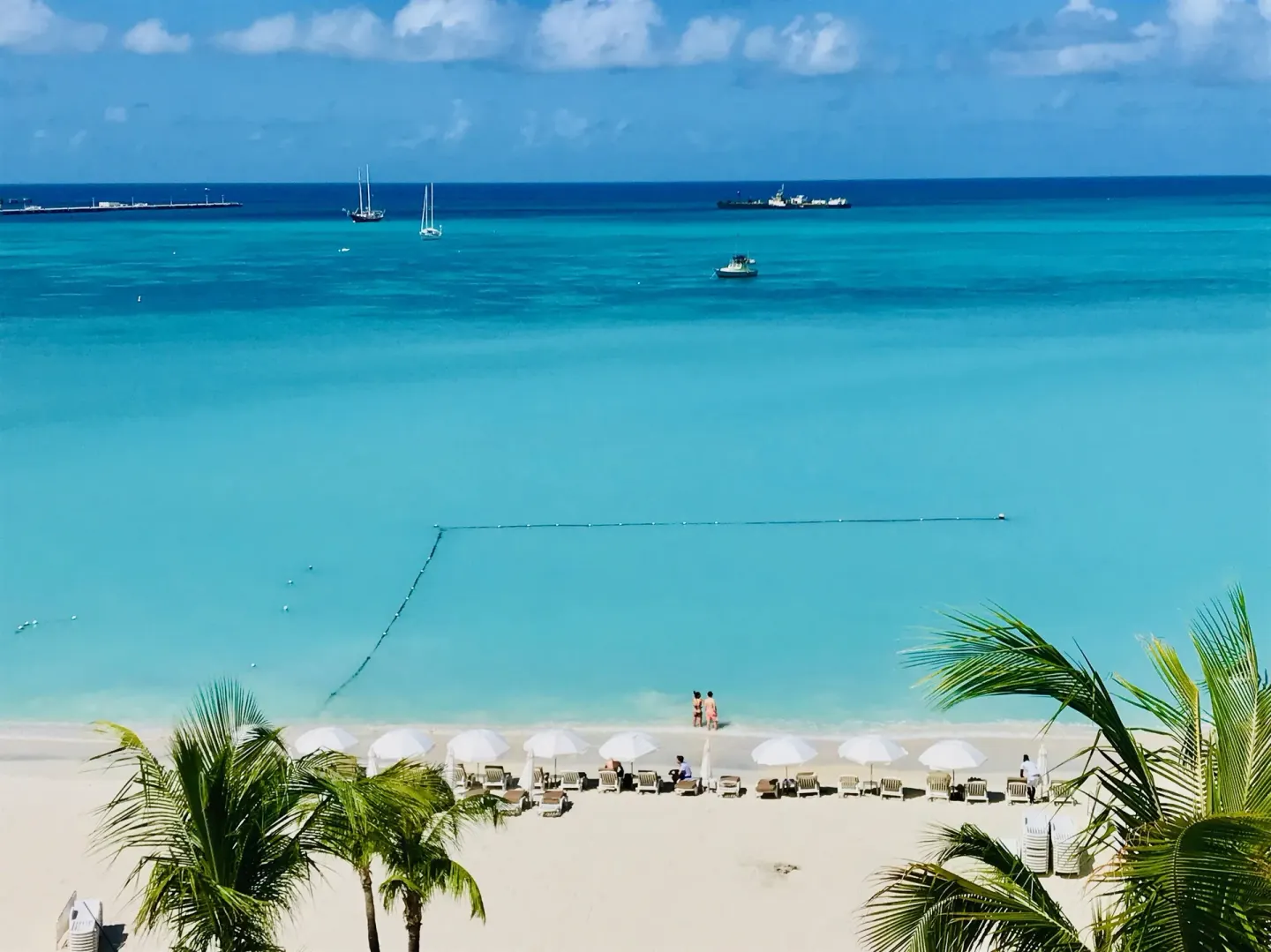 Beach and turquoise sea view from Holland House Beach Hotel with loungers and boats.