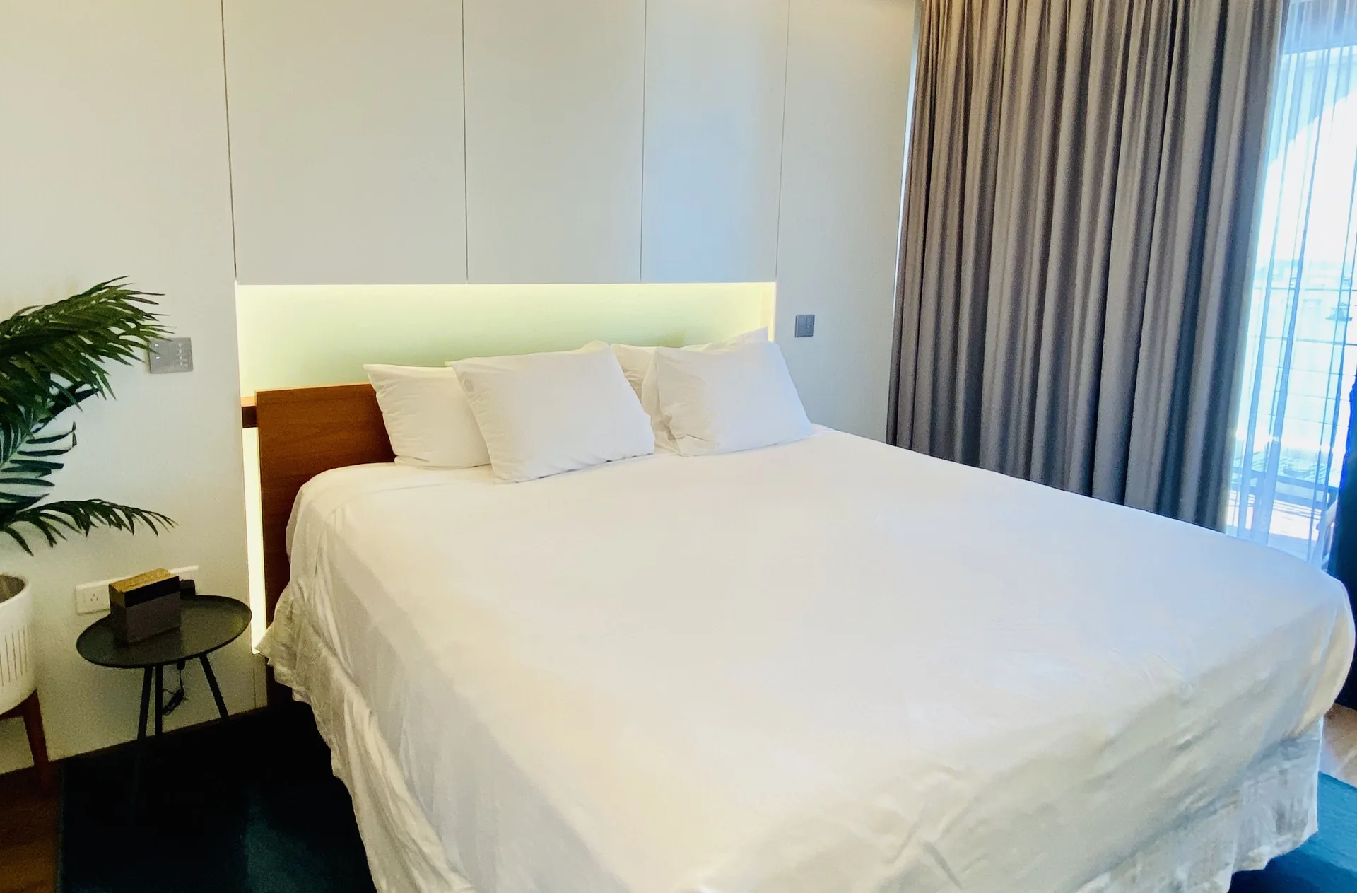 Royal Studio Suite bed with white linens and balcony curtains at Holland House Beach Hotel.