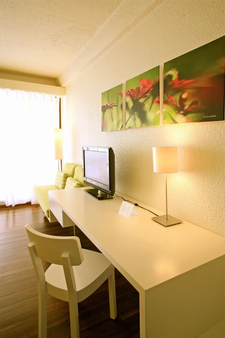 Superior Room City View desk, TV, sofa, and floral wall art at Holland House Beach Hotel.
