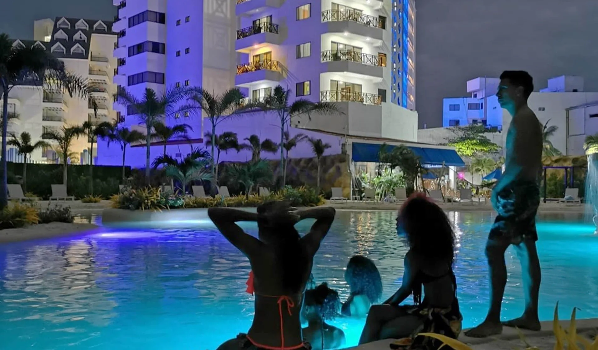 Evening pool scene with guests and colorful lighting at Hotel Arena Blanca.