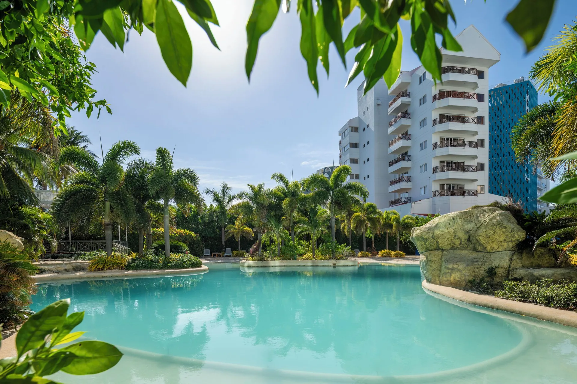 Lagoon pool framed by leafy branches and hotel towers at Hotel Arena Blanca.