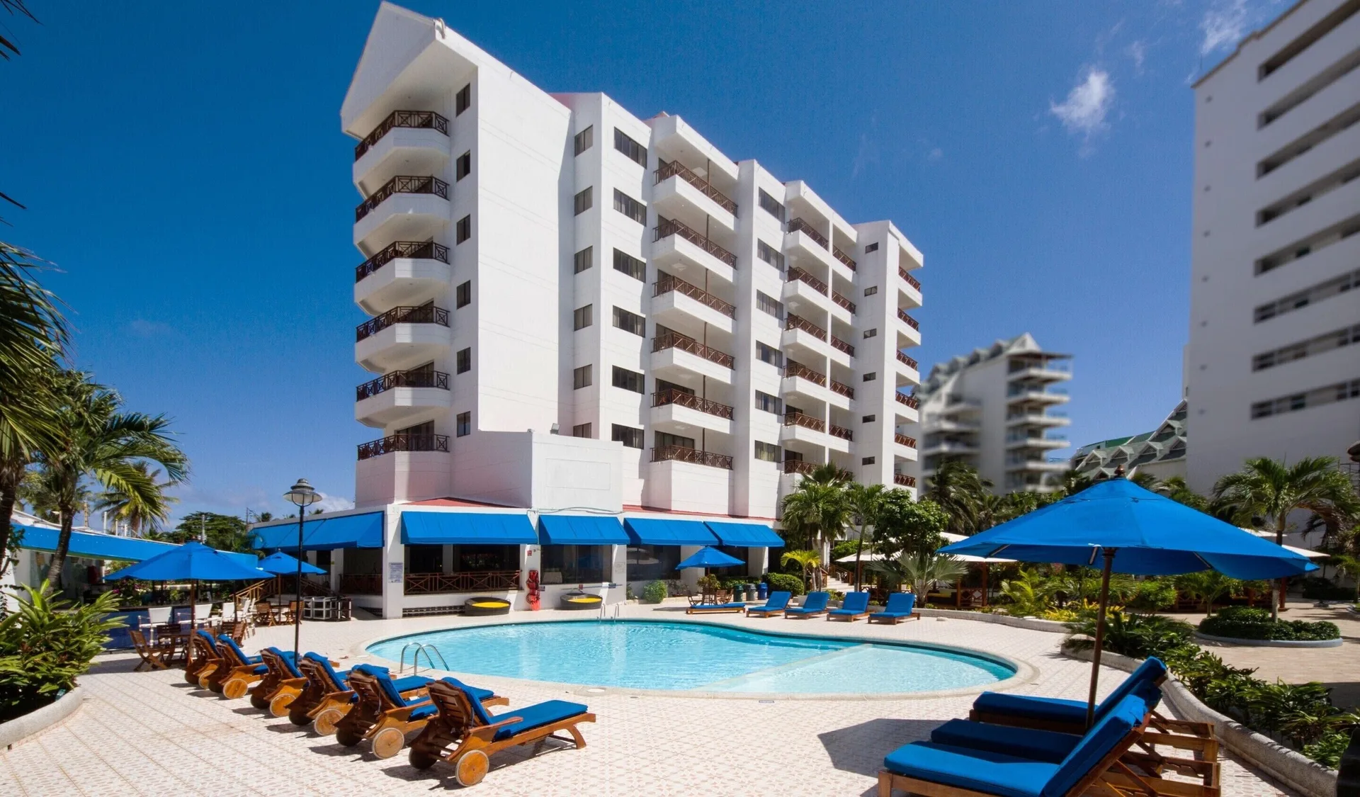 Outdoor pool with blue loungers, umbrellas, and white balconies at Hotel Arena Blanca.