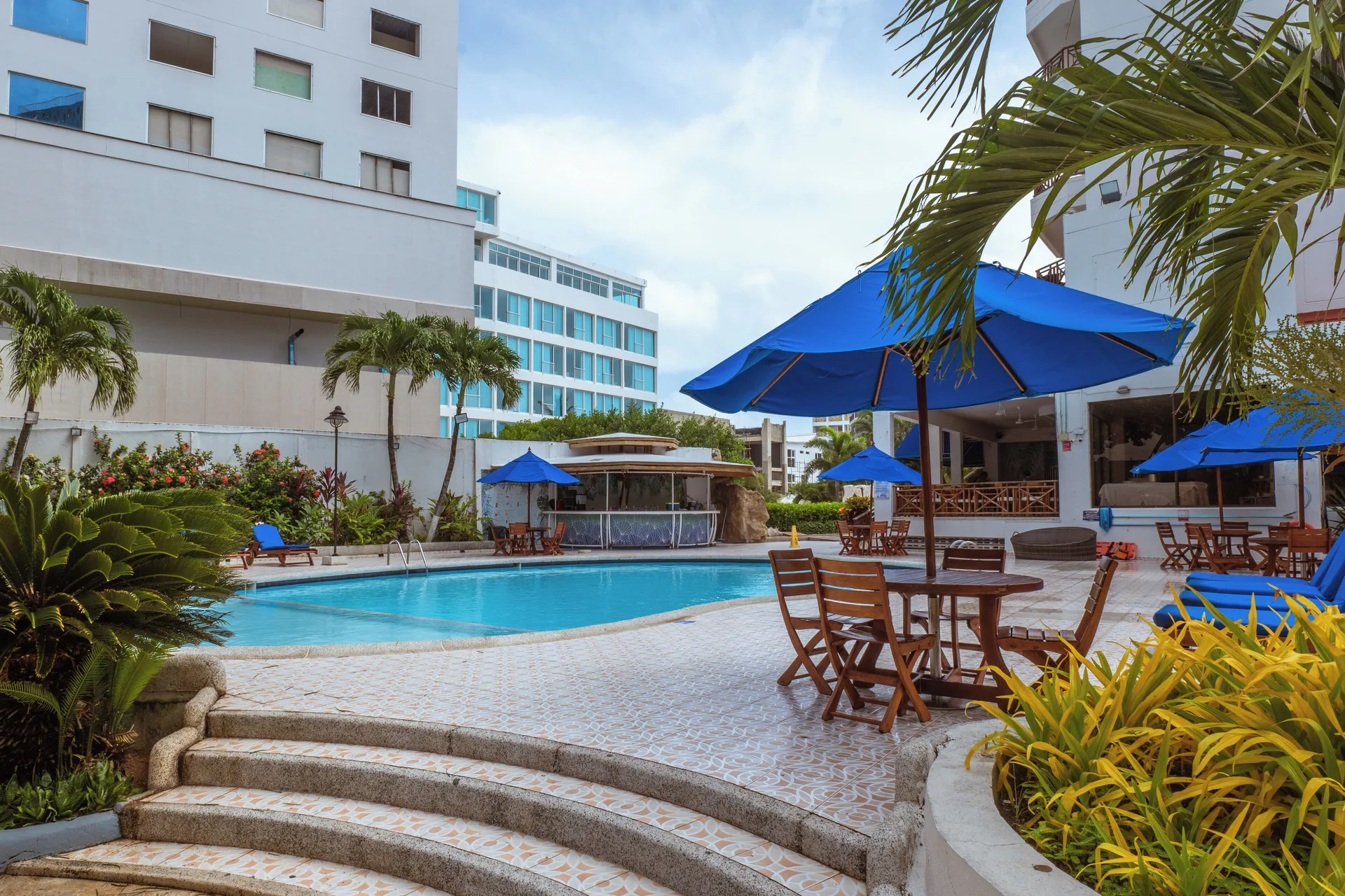 Pool terrace with blue umbrellas, tables, and tropical plants at Hotel Arena Blanca.