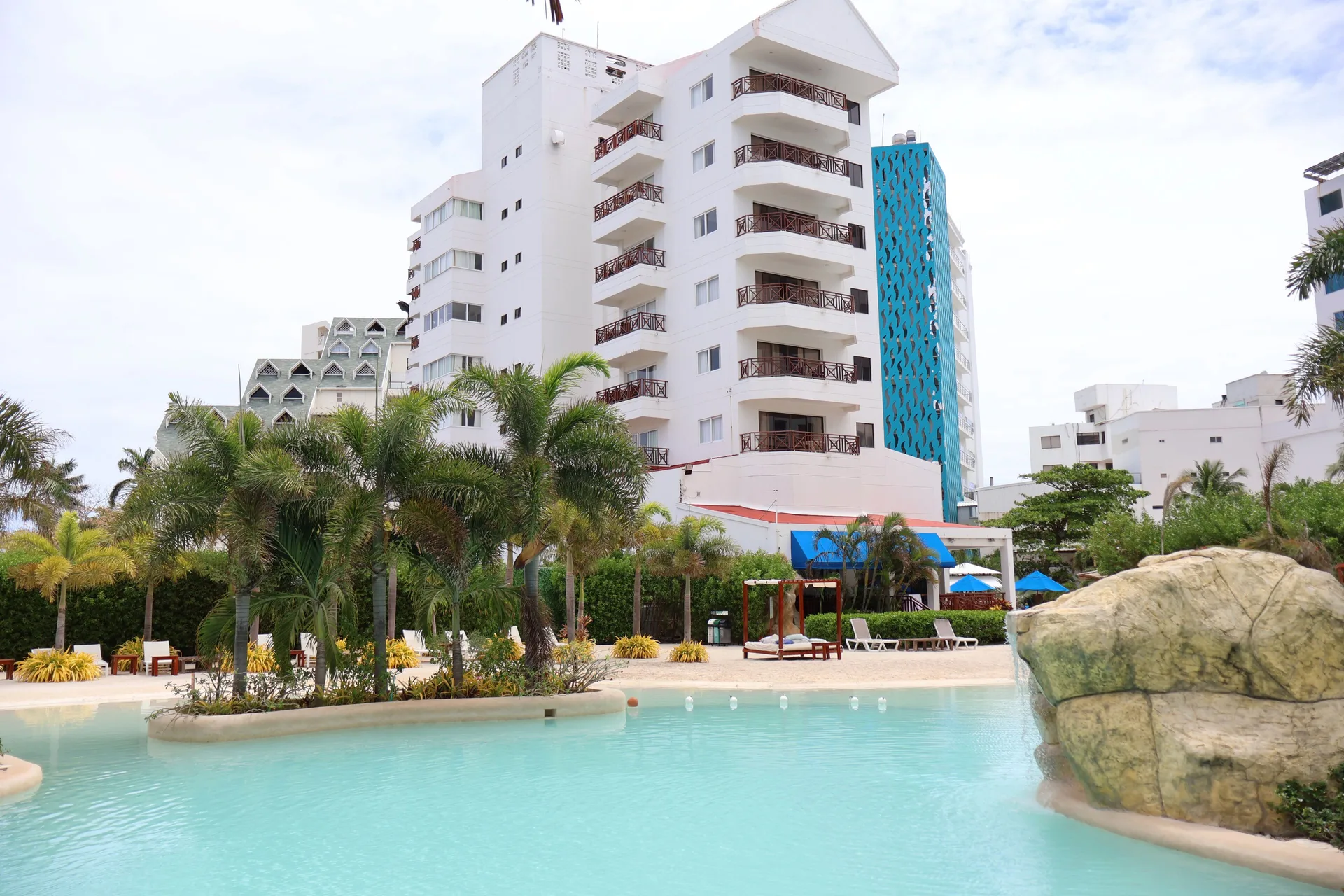 Poolside palms, rock feature, and white building at Hotel Arena Blanca.