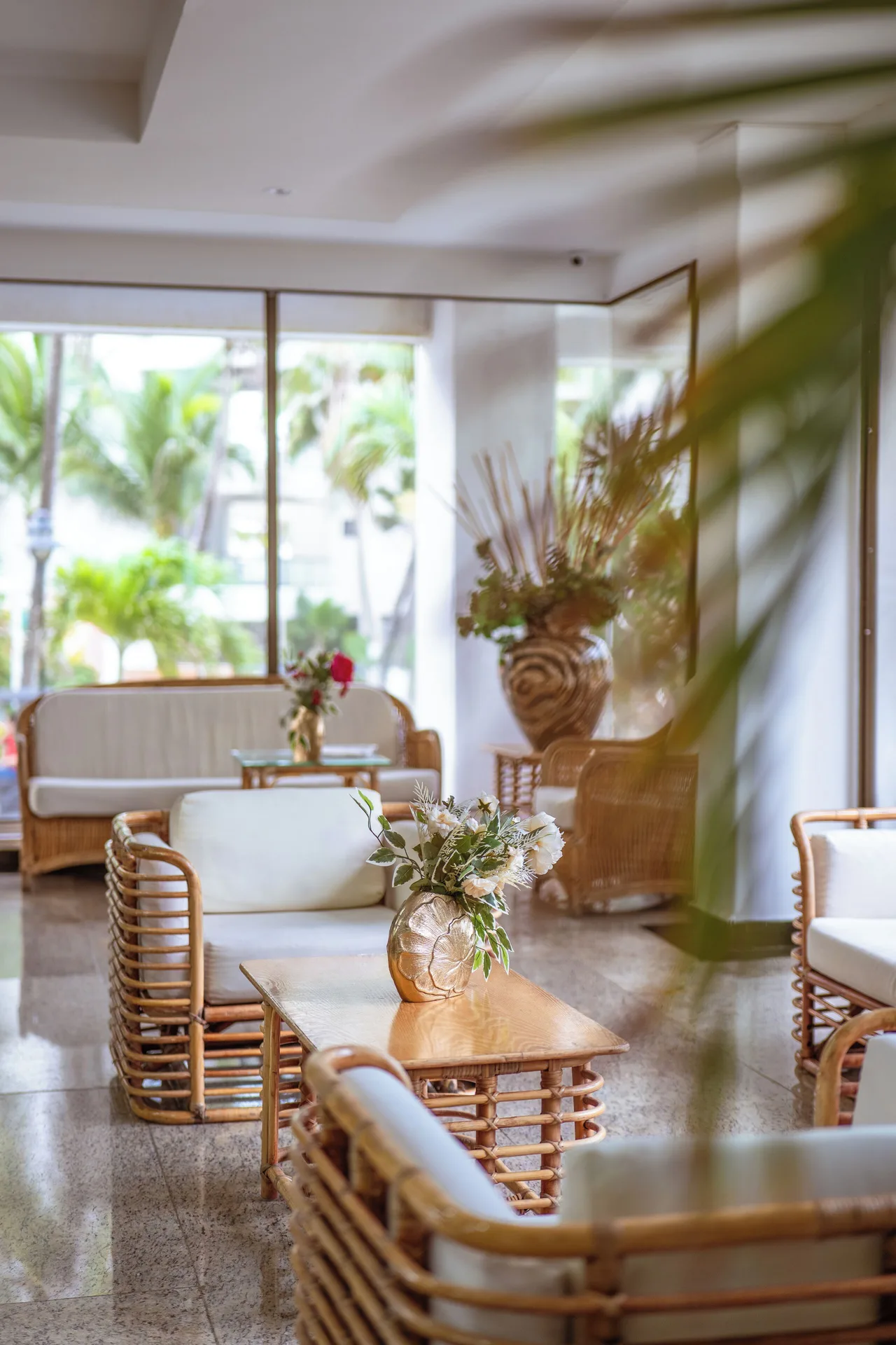 Rattan lobby seating with flower arrangements and palm views at Hotel Arena Blanca.