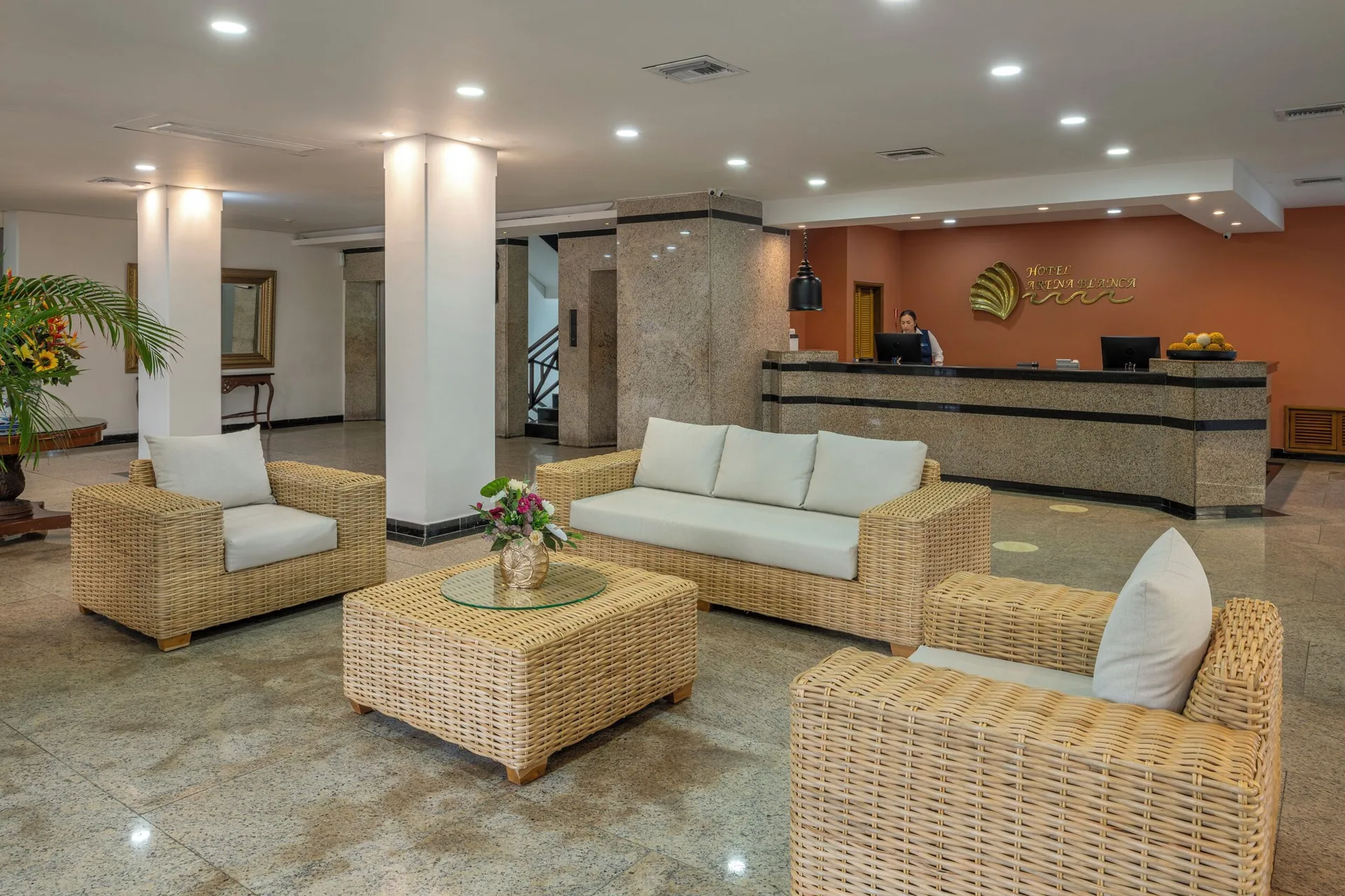 Reception desk with wicker lounge seating and white cushions at Hotel Arena Blanca.