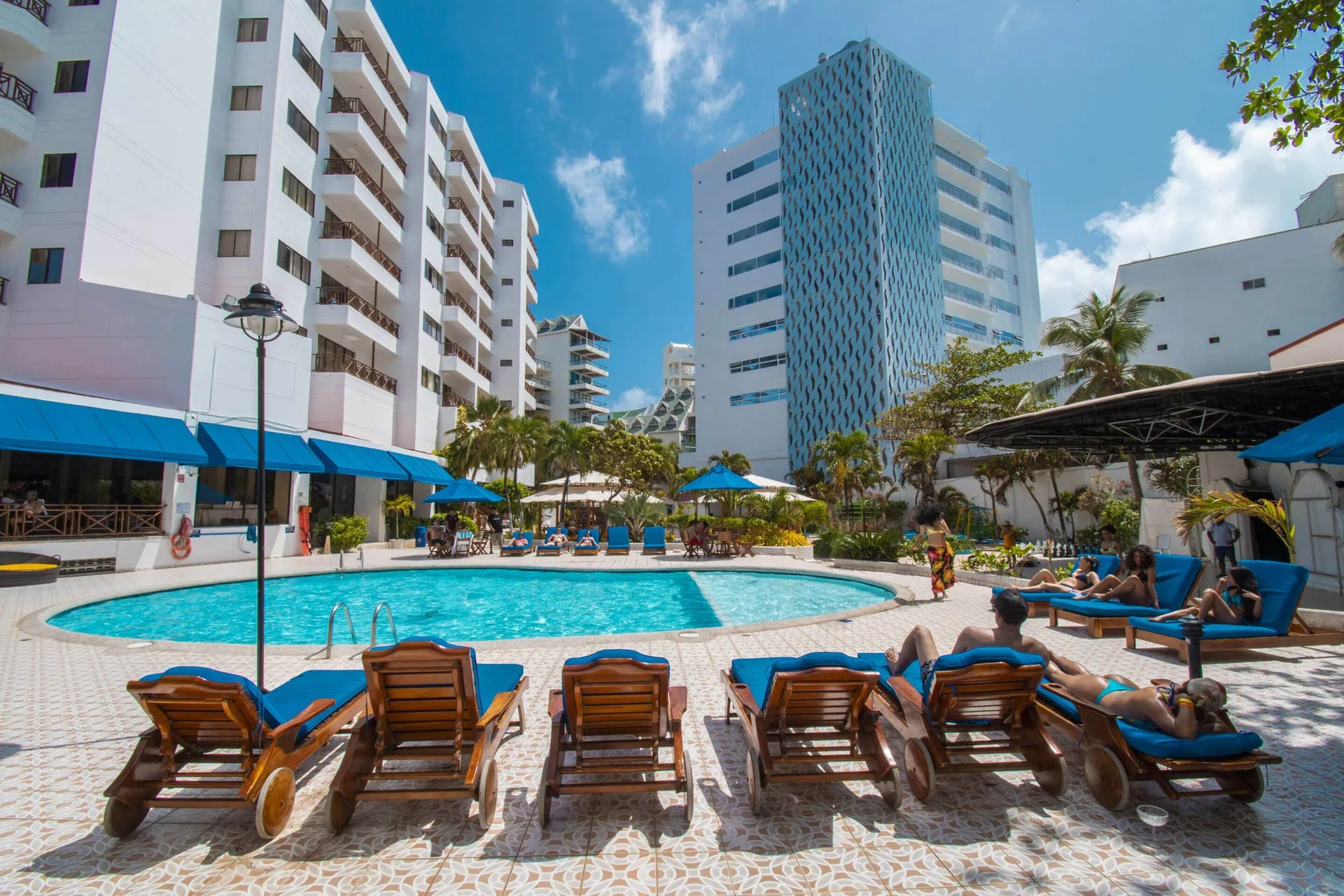 Sunny pool deck with guests on blue-cushioned loungers at Hotel Arena Blanca.