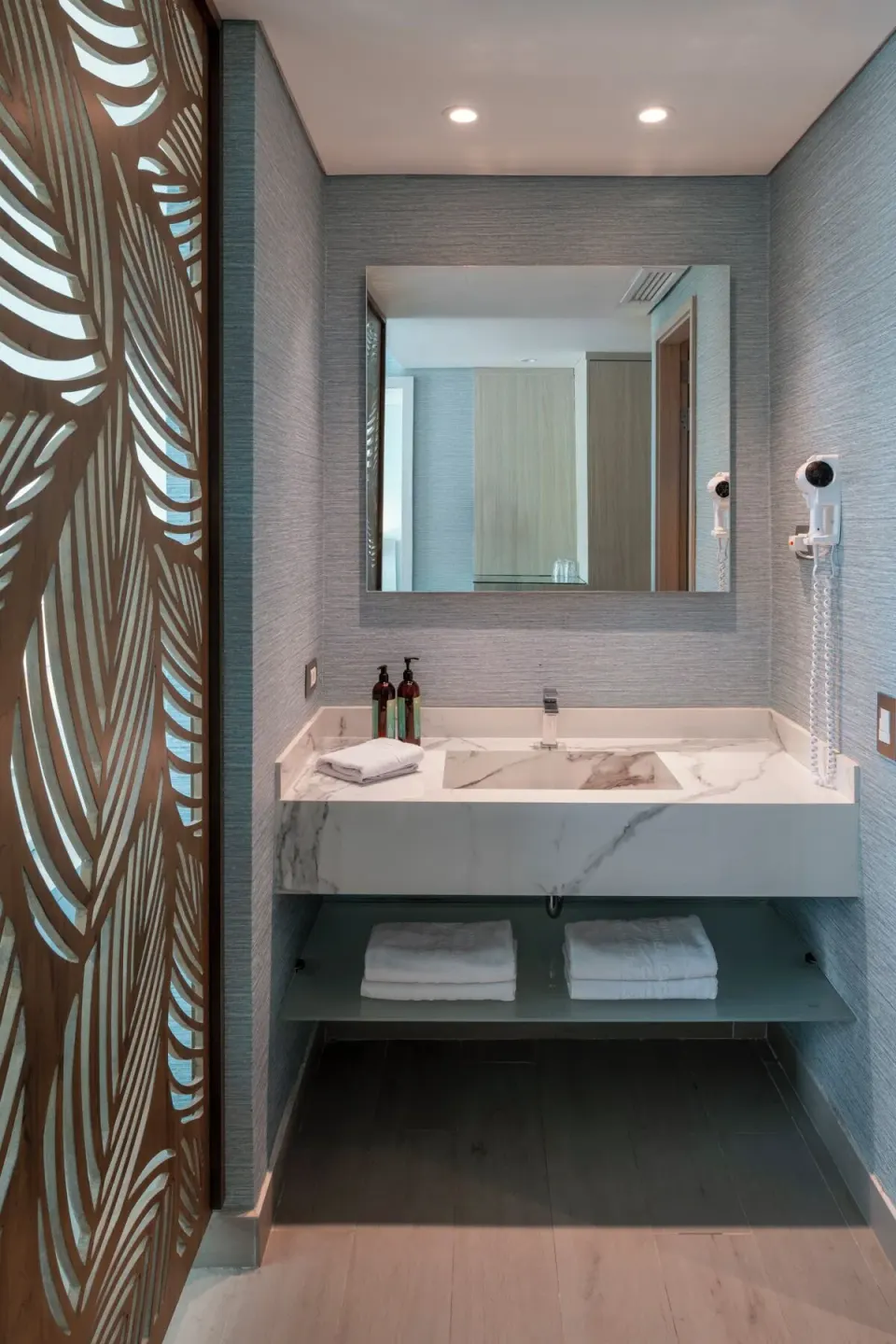 Superior Room bathroom vanity with mirror, towels, bottles, and leaf partition at Hotel Arena Blanca.