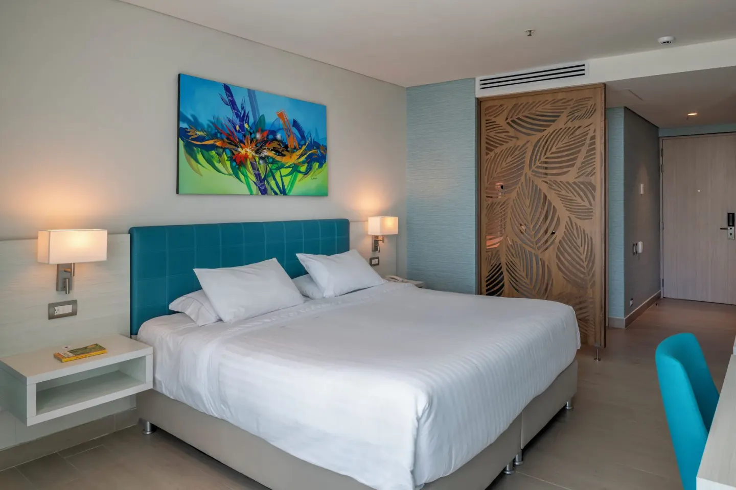 Superior Room king bed with teal headboard, artwork, lamps, and entry area at Hotel Arena Blanca.