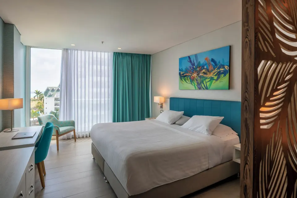 Superior Room king bed, desk, chair, window, and teal curtains at Hotel Arena Blanca.