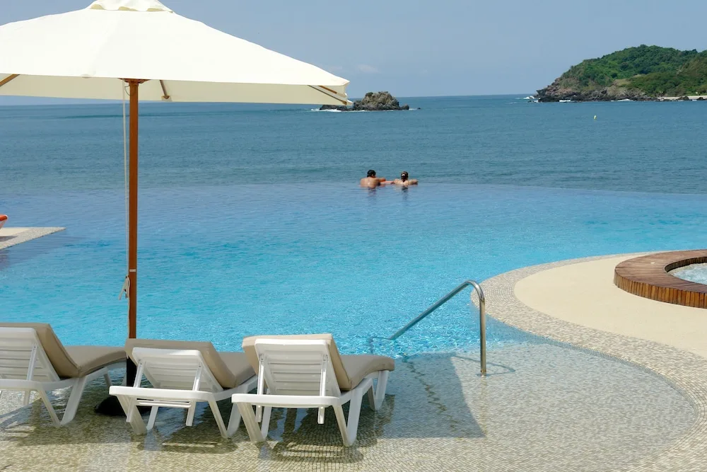 Infinity pool with loungers, umbrella, and ocean view at Hotel Azul Ixtapa Grand Resort Spa.