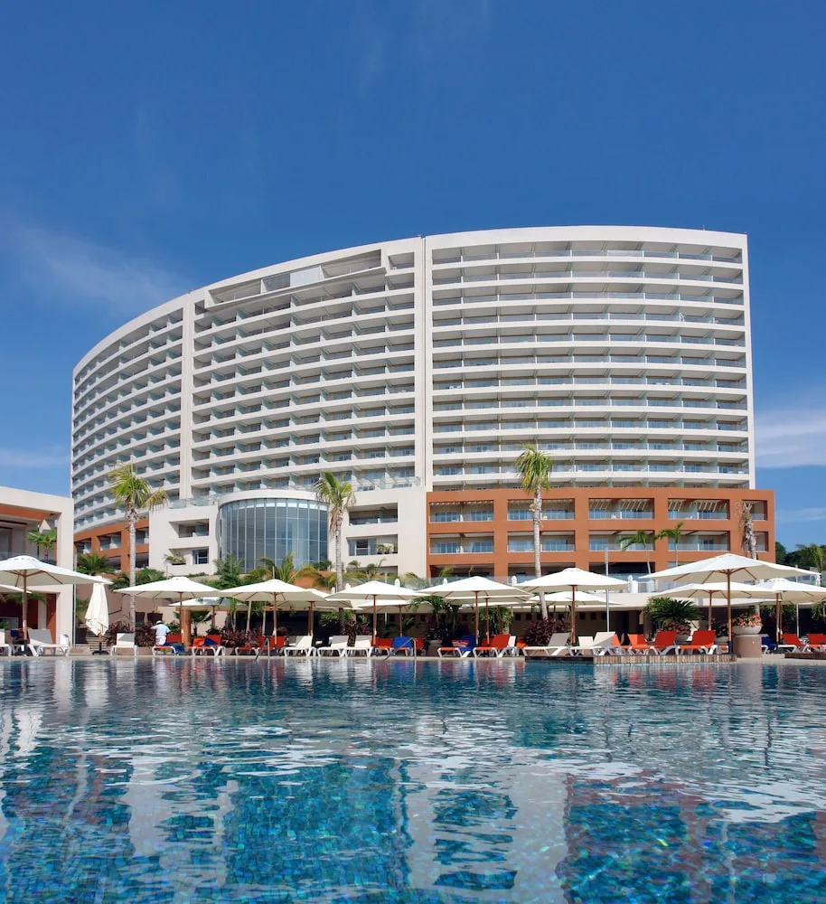 Curved resort tower and pool with umbrellas at Hotel Azul Ixtapa Grand Resort Spa.