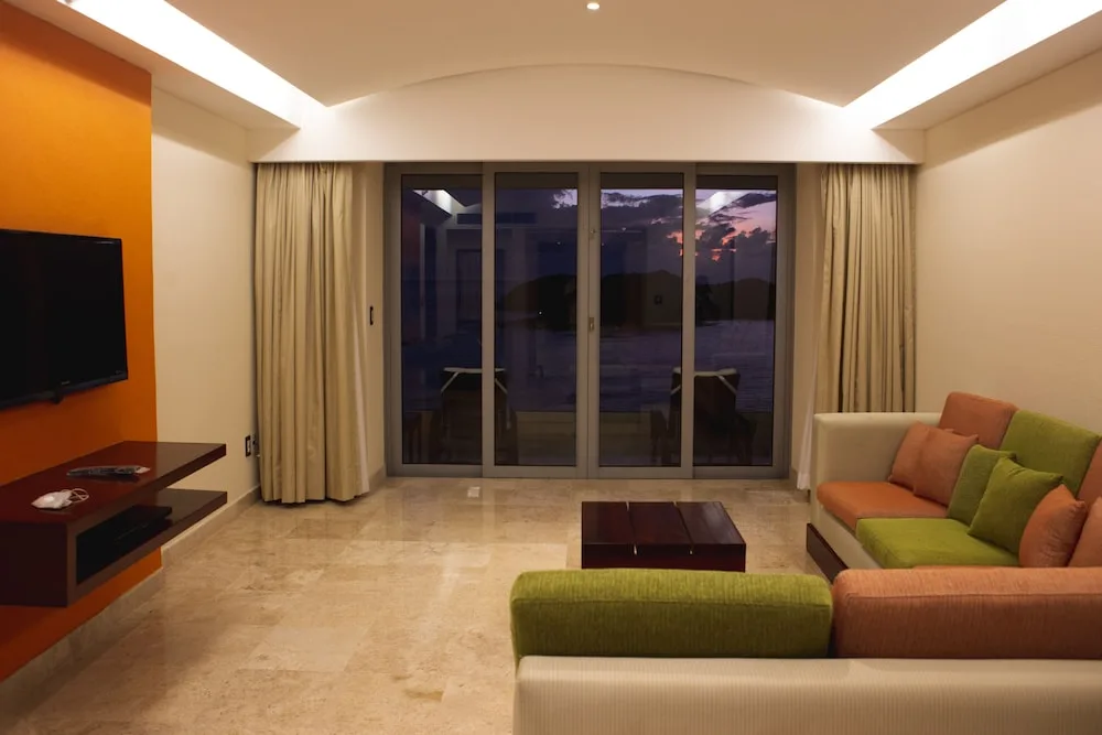 Suite living room with sofas, TV, and balcony doors at Hotel Azul Ixtapa Grand Resort Spa.