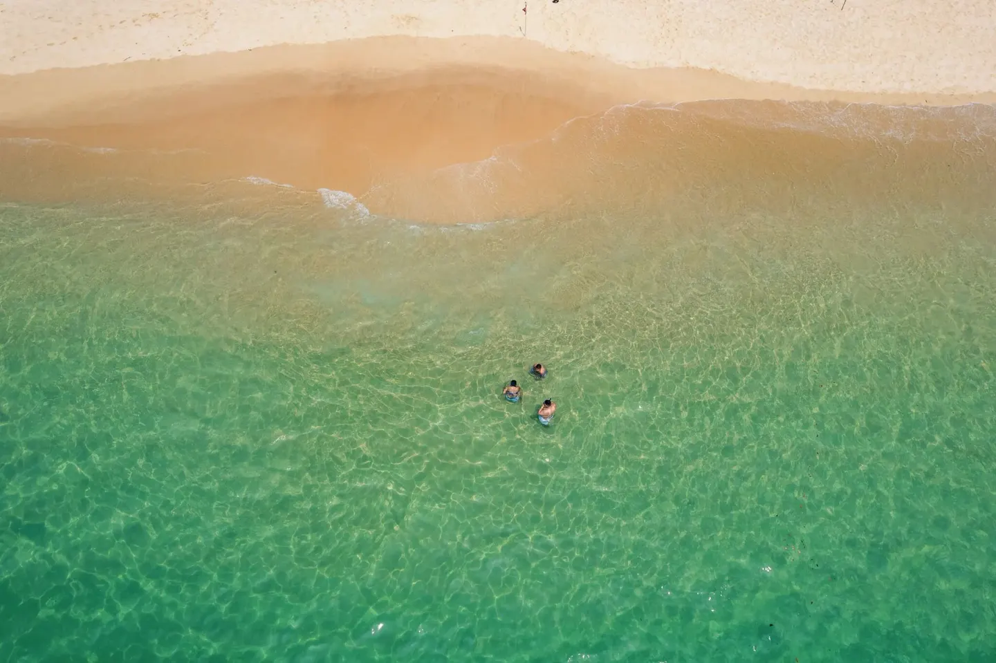 Aerial view of swimmers in clear green water by the beach at Hotel Castillo Huatulco & Beach Club.