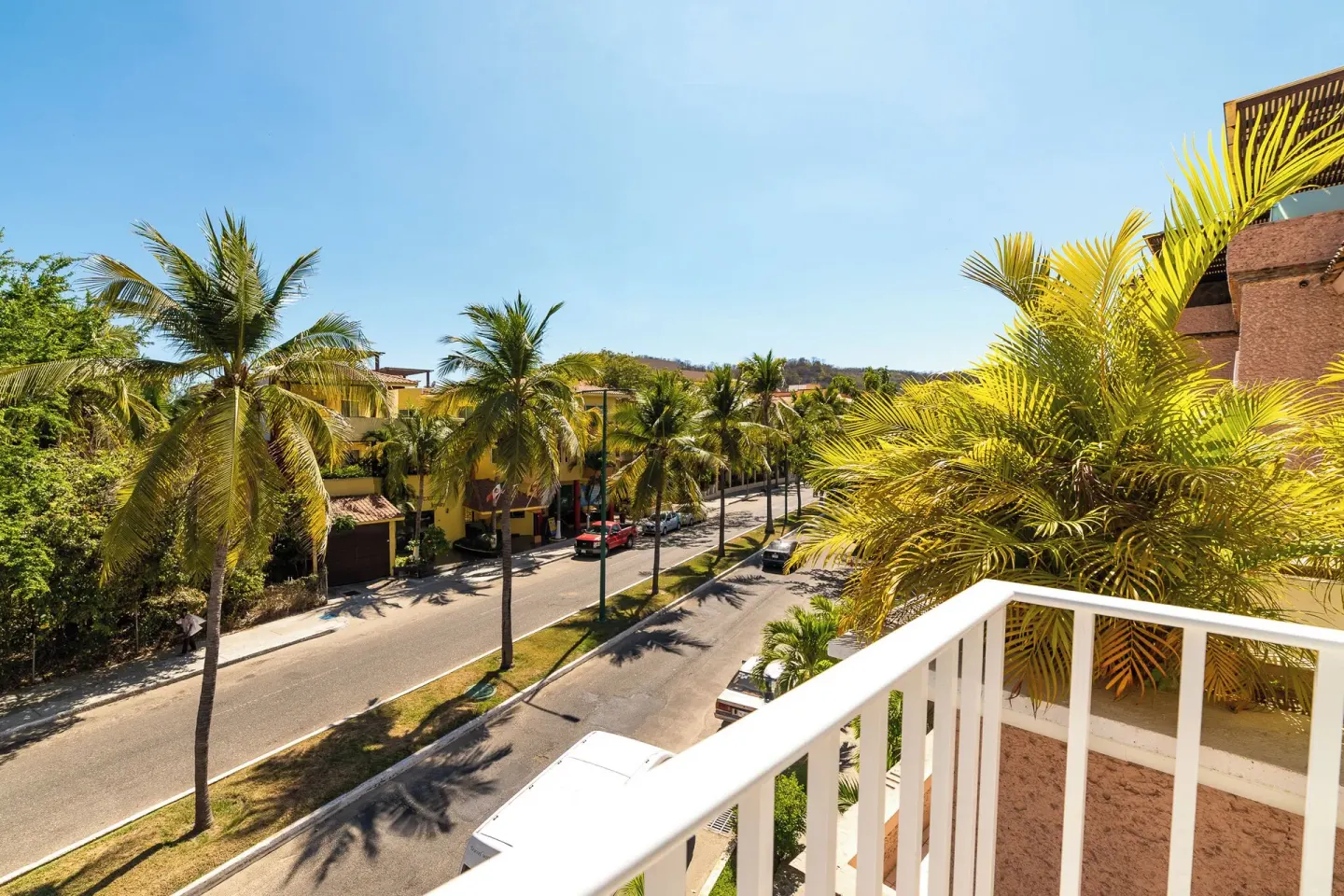 Balcony overlooking palms and a quiet street at Hotel Castillo Huatulco & Beach Club.