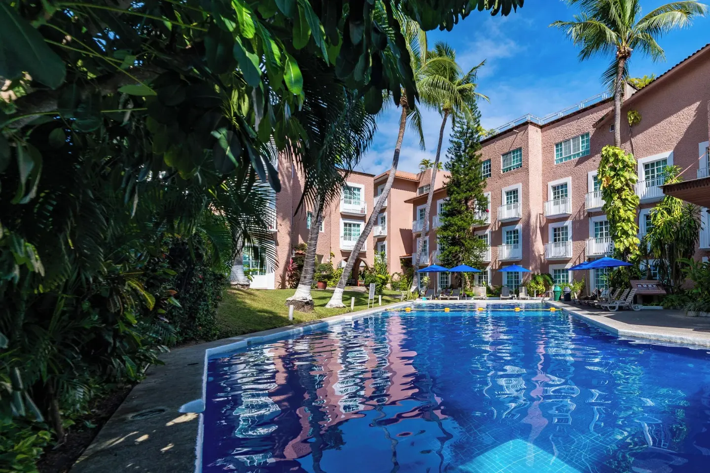Courtyard pool bordered by palms and guest room buildings at Hotel Castillo Huatulco & Beach Club.