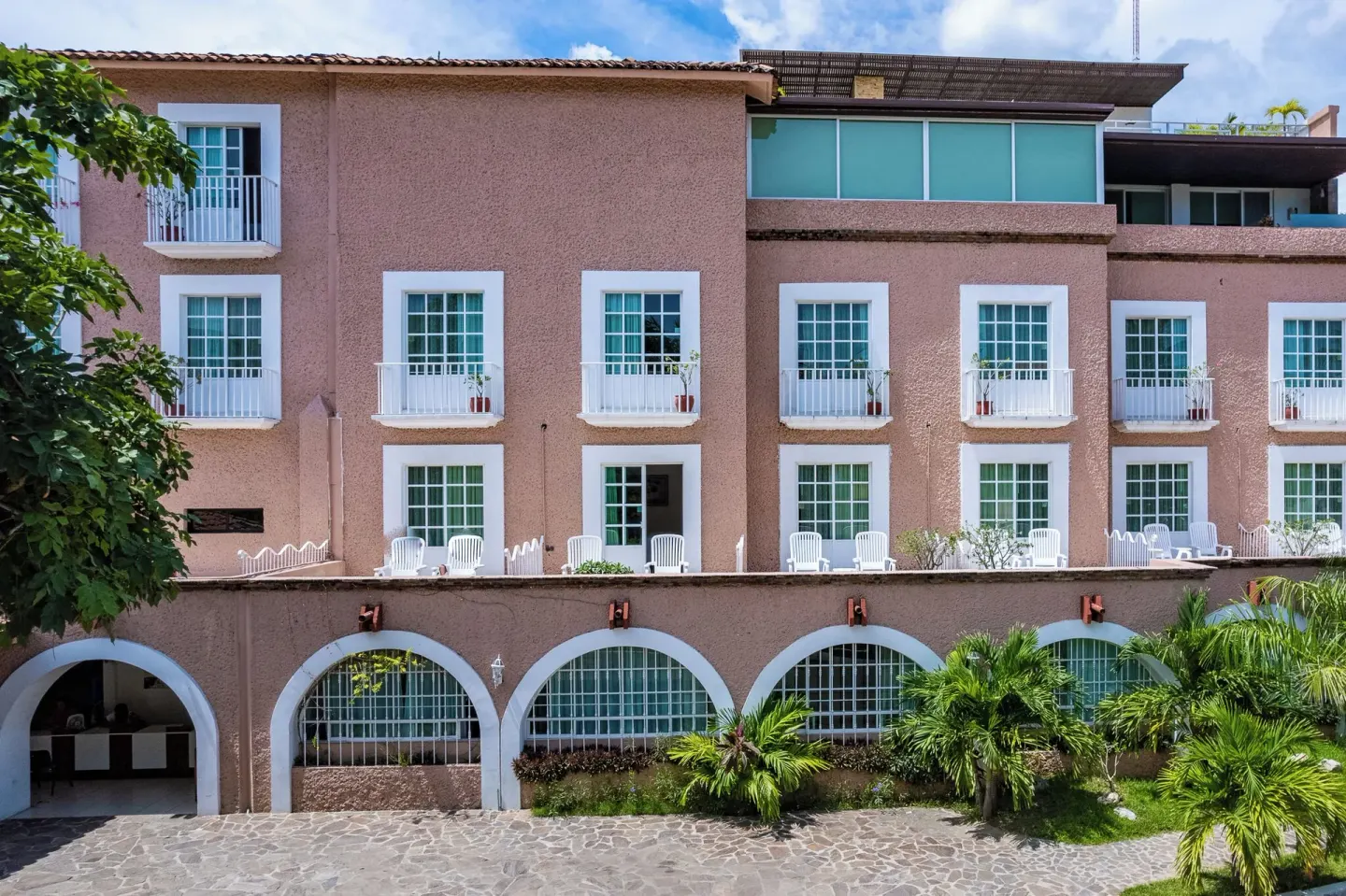 Exterior facade at Hotel Castillo Huatulco & Beach Club with arched openings, balconies, and palms.