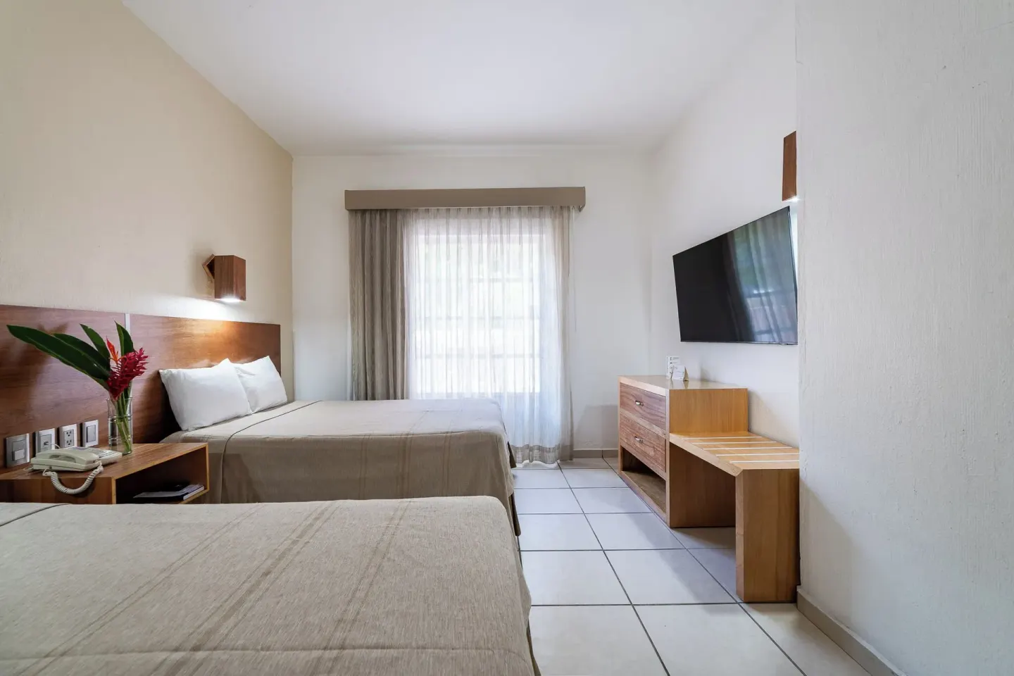Guest room with two beds, wood furniture, and wall-mounted TV at Hotel Castillo Huatulco & Beach Club.