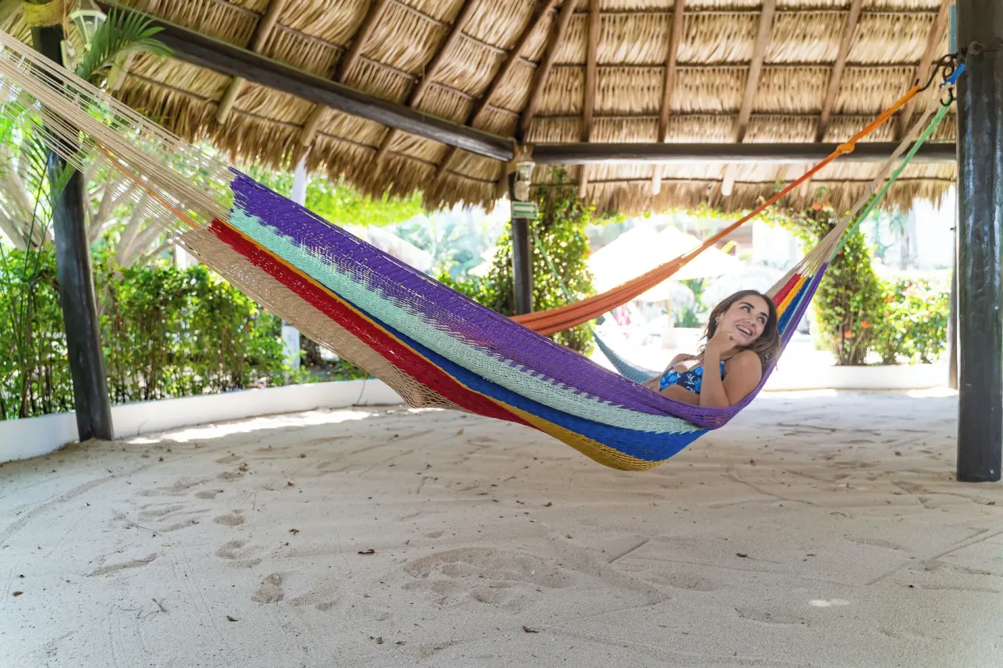 Guest relaxing in a colorful hammock under a thatched shelter at Hotel Castillo Huatulco & Beach Club.