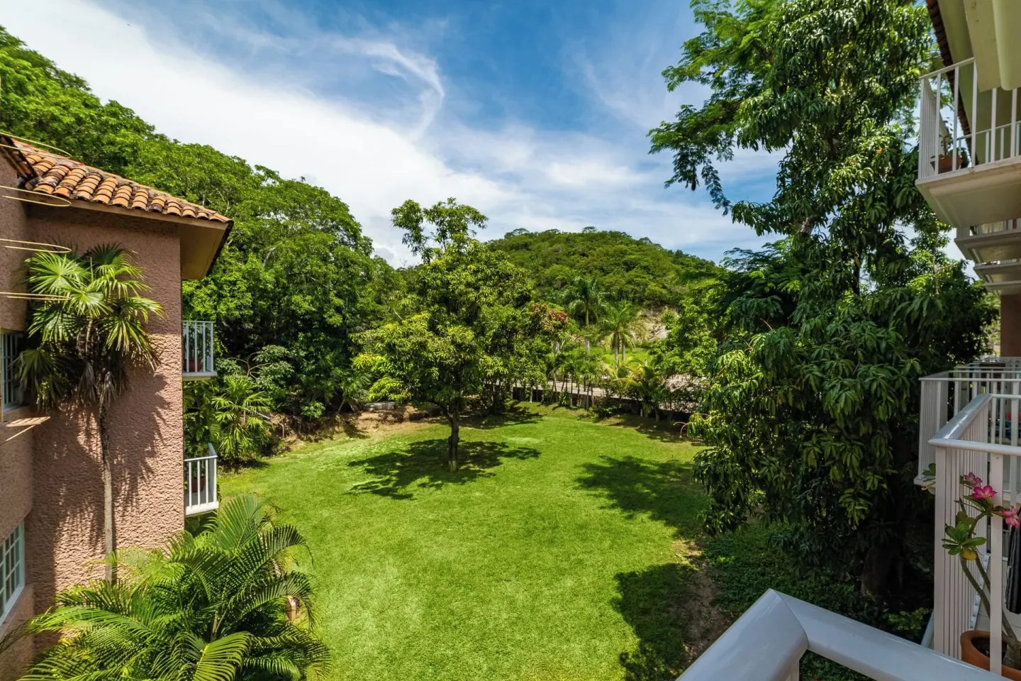 Lawn and tropical trees at Hotel Castillo Huatulco & Beach Club between guestroom balconies.