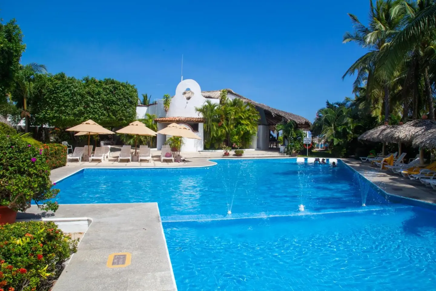 Outdoor pool with fountains and loungers at Hotel Castillo Huatulco & Beach Club.